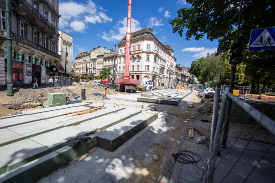 Prace budowlane na ulicy, widoczne maszyny i robotnicy, nieukończona nawierzchnia.