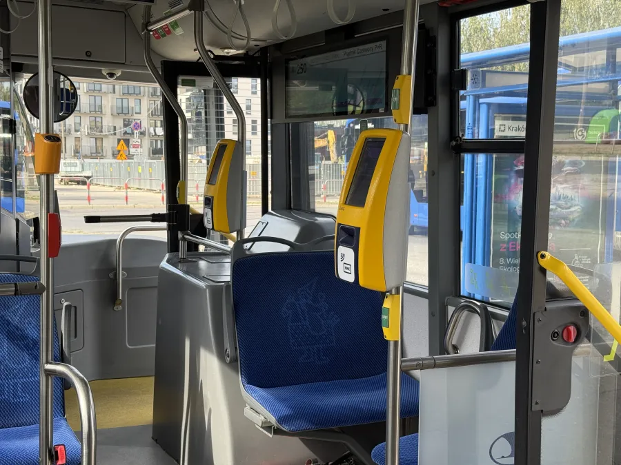 Wnętrze autobusu z żółtymi kasownikami i niebieskimi siedzeniami.