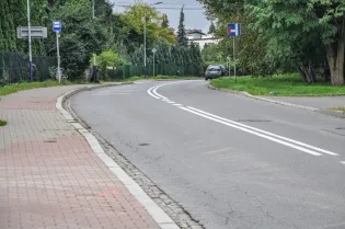 Droga z zakrętem, chodnik, przystanek autobusowy i zaparkowany samochód.