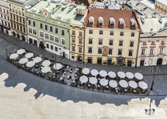 Kawiarniane parasole na rynku, otoczone kolorowymi budynkami.