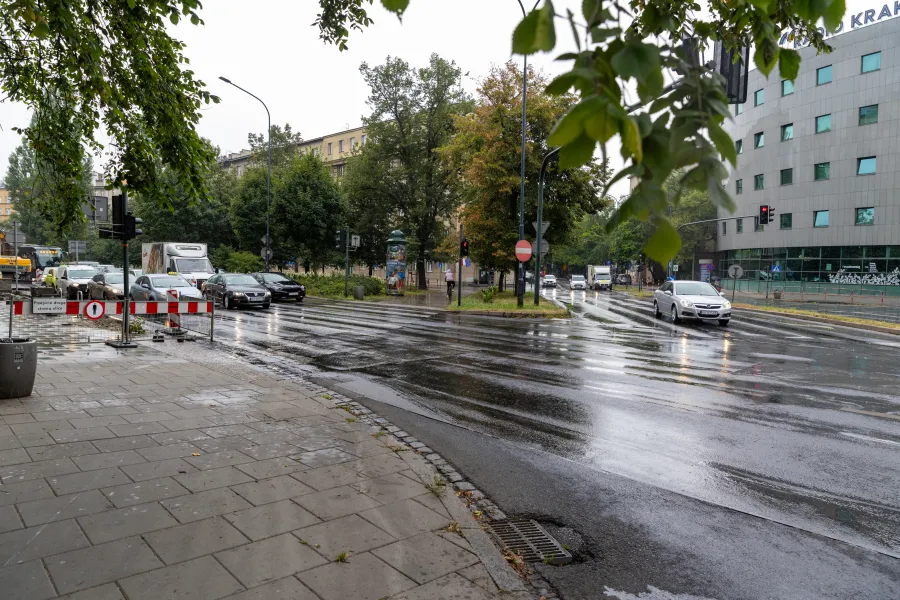 Deszczowa ulica z samochodami, sygnalizacją świetlną i mokrym asfaltem.