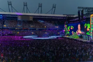 Tłum ludzi na koncercie z kolorową sceną i ekranem w tle.