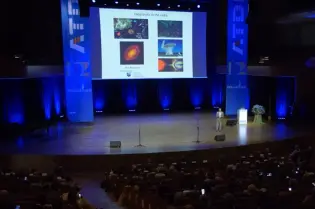 Prezentacja na konferencji z wykładowcą i slajdami w tle.