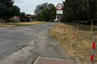 Droga z ograniczeniem wysokości do 3,5 m, otoczona drzewami i ogrodzeniem.