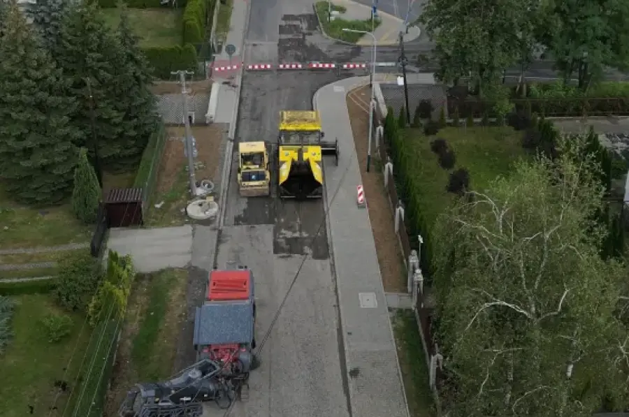 Prace drogowe na ulicy, widok na maszynę budowlaną i otoczenie.
