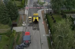 Prace drogowe na ulicy, widok na maszynę budowlaną i otoczenie.