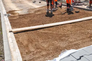 Prace budowlane na placu, przygotowanie podłoża z żwiru.
