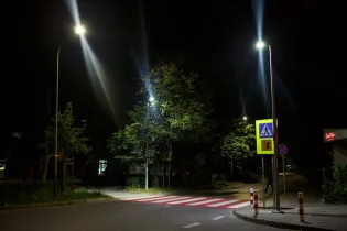 Oświetlona ulica nocą z przejściem dla pieszych i znakami drogowymi.