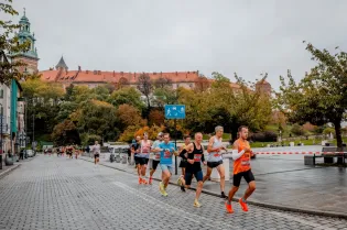Biegacze na ulicy w mieście, w tle zamek i drzewa w jesiennych kolorach.
