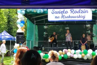 Występ artystyczny na festynie rodzinnym z muzykami i dekoracjami w tle.