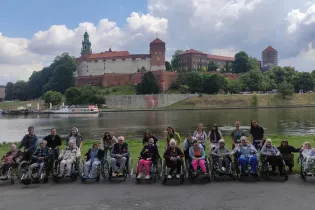 Grupa osób na wózkach inwalidzkich przed zamkiem na wzgórzu Wawelskim.