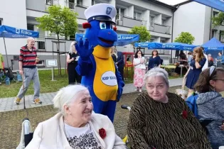 Maskotka w mundurze policjanta wita seniorów na wydarzeniu plenerowym.