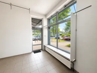 Pusty lokal z dużymi oknami, widok na parking i drzewa za oknem.