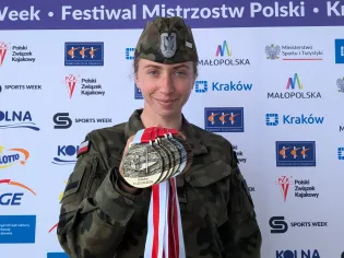 Kobieta w mundurze wojskowym trzyma medale, stoi na tle banerów festiwalu.