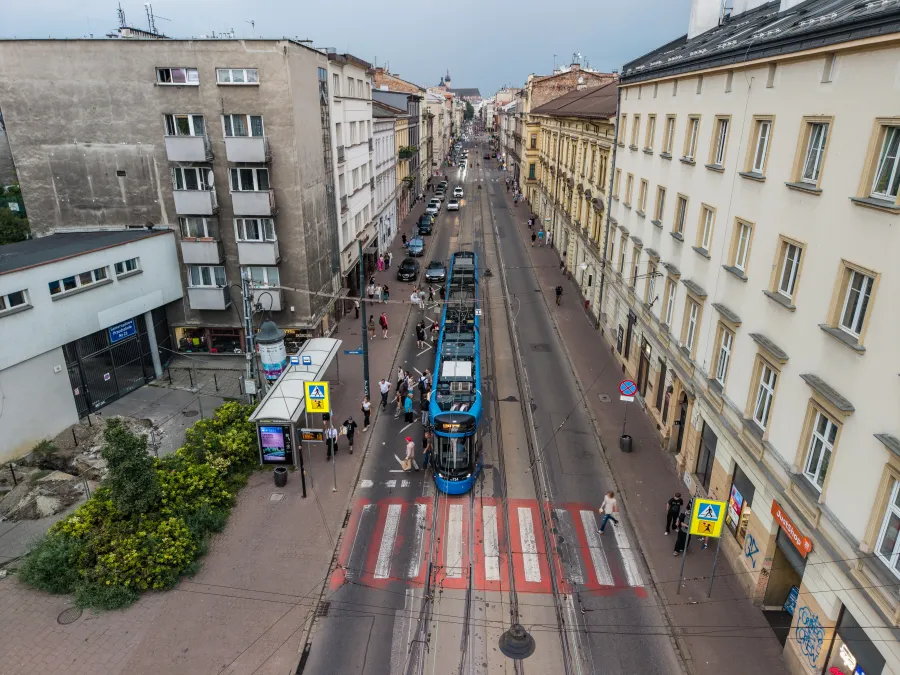 Tramwaj na ulicy z budynkami mieszkalnymi i samochodami zaparkowanymi po obu stronach.