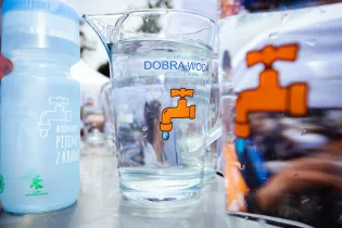 Szklanka z wodą i butelka z napisem Dobra Woda, symbol kranu.