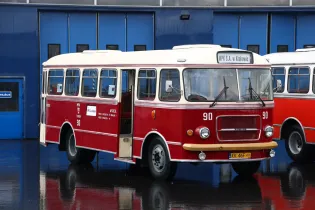 Czerwony autobus z numerem 90, z logo MPS S.A. w Krakowie, zaparkowany przed budynkiem.