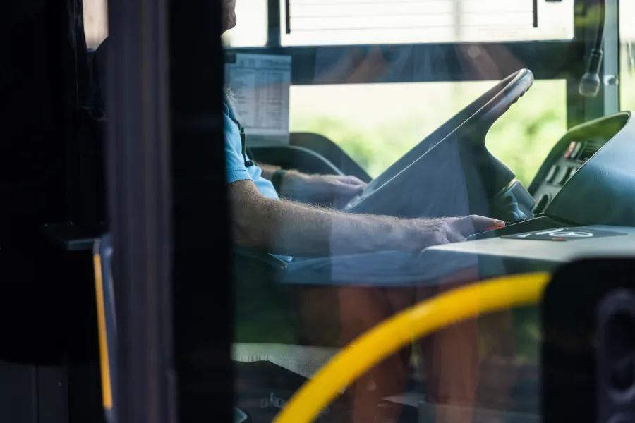 Kierowca autobusu siedzący za kierownicą, widok z wnętrza pojazdu.