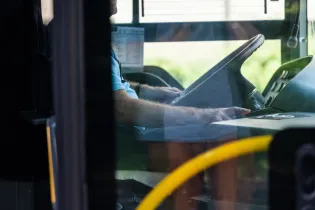 Kierowca autobusu siedzący za kierownicą, widok z wnętrza pojazdu.