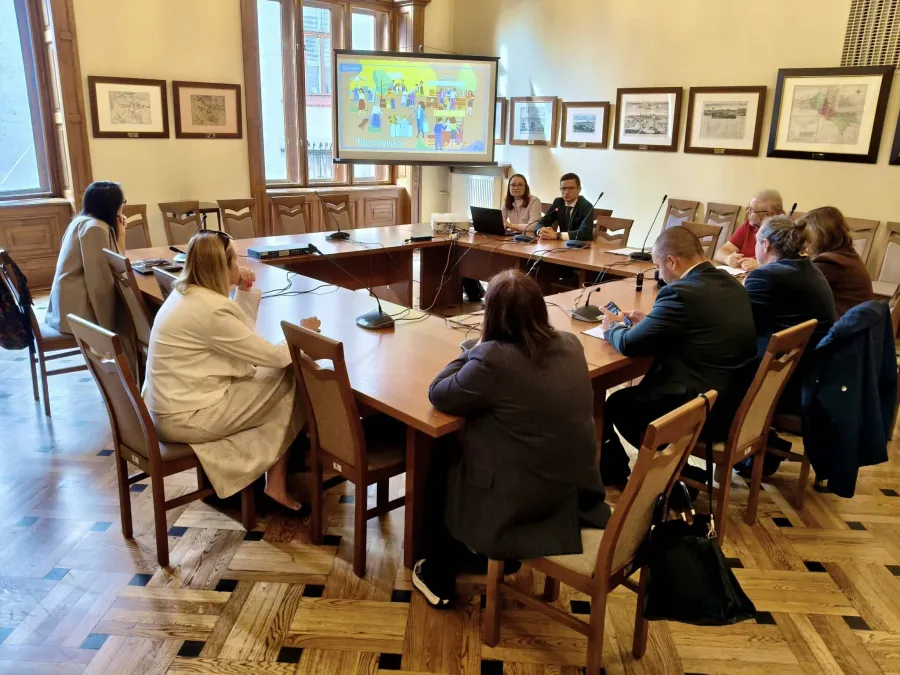 Spotkanie w sali konferencyjnej z prezentacją na ekranie i uczestnikami przy stole.
