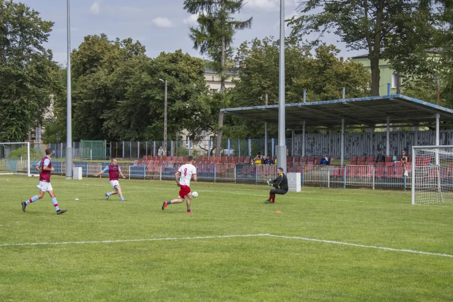 Mecz piłki nożnej na boisku, zawodnicy w akcji, bramkarz przygotowany do obrony.