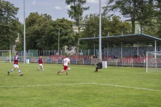 Mecz piłki nożnej na boisku, zawodnicy w akcji, bramkarz przygotowany do obrony.