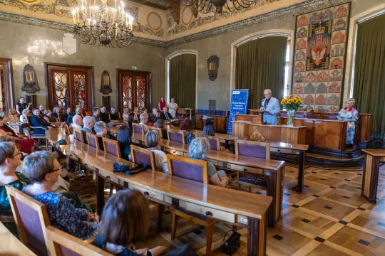 Uroczystość w sali z publicznością i mówcą przy mównicy.