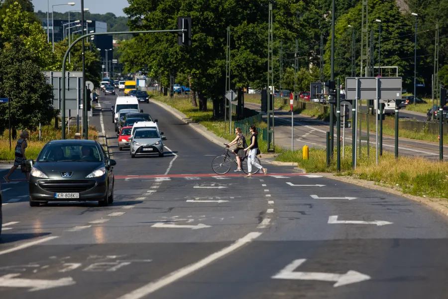 Ruch uliczny z pieszymi i rowerzystą na przejściu dla pieszych.