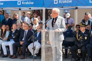 Mężczyzna w garniturze przemawia do zgromadzonego tłumu podczas wydarzenia w Krakowie.