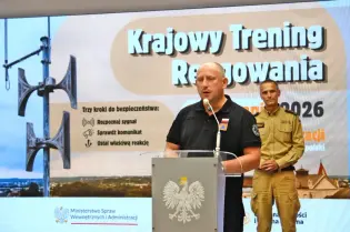 Mężczyzna przemawia przy mównicy, w tle plakat dotyczący krajowego treningu reagowania.
