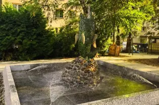 Fontanna z rzeźbą drzewa w parku, otoczona zielenią i kamieniami.