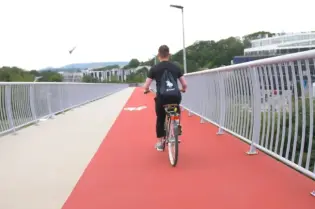 Mężczyzna na rowerze jedzie po czerwonym chodniku rowerowym.