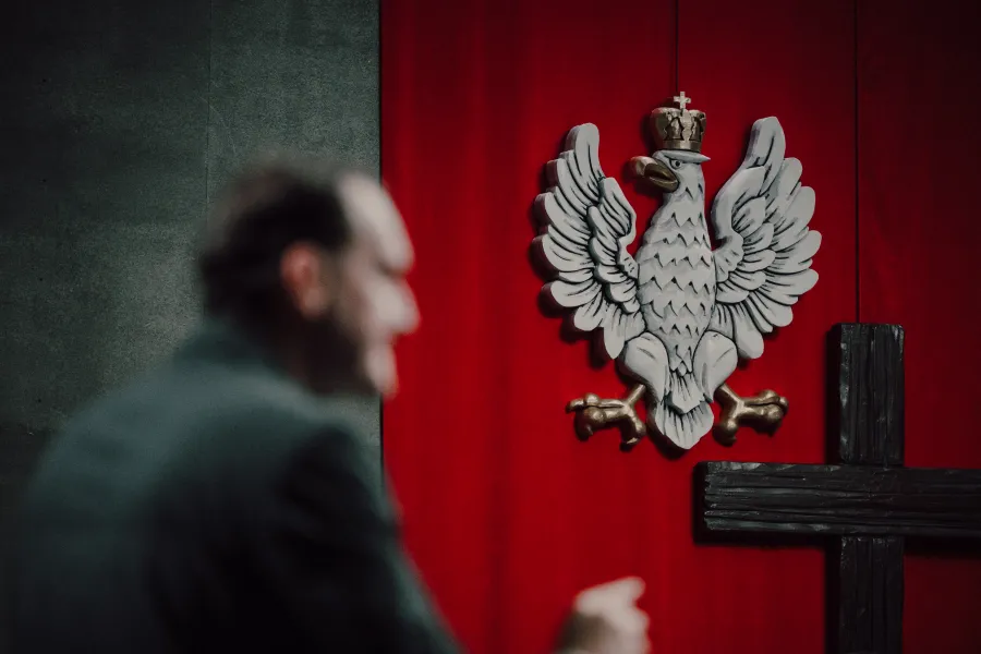 Orzeł biały na czerwonym tle z krzyżem w tle.