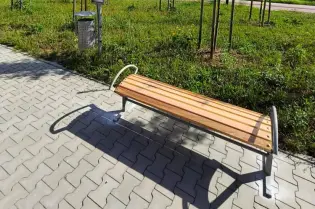 Ławka na przystanku autobusowym z zielenią w tle i niebieskim znakiem przystanku.