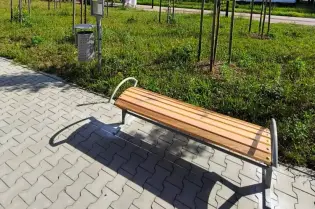 Ławka na przystanku autobusowym z zielenią w tle i niebieskim znakiem przystanku.