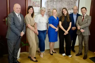 Grupa osób w formalnych strojach, pozująca do zdjęcia w biurze.