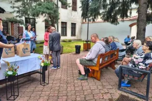Spotkanie w ogrodzie z uczestnikami siedzącymi na ławkach, przy stole z darami.