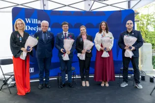 Uroczystość wręczenia odznaczeń, uczestnicy z bukietami kwiatów.
