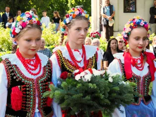 Trzy dziewczynki w tradycyjnych strojach ludowych z kwiatowymi wiankami na głowach.