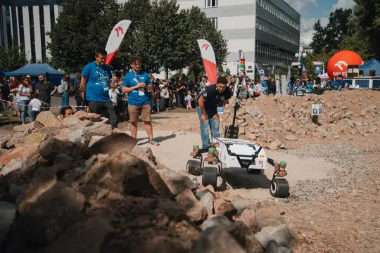 Robot poruszający się po terenie z kamieniami, z uczestnikami wydarzenia w tle.