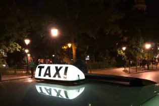 Taksa na dachu samochodu w oświetlonym parku nocą.