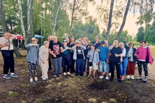 Grupa osób w różnym wieku pozująca na świeżym powietrzu w parku.
