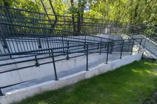 Widok na betonowe schody z barierkami otoczone zielenią.