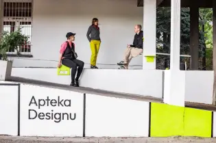 Cztery osoby w różnych strojach siedzą i rozmawiają w przestrzeni publicznej z napisem Apteka Designu.
