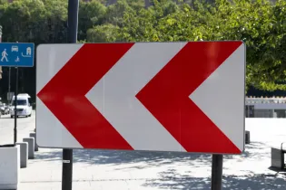 Znak drogowy z trzema czerwonymi strzałkami w lewo.