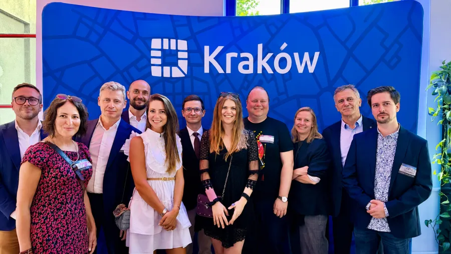Grupa osób pozujących przed tłem z napisem Kraków.
