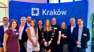 Grupa osób pozujących przed tłem z napisem Kraków.