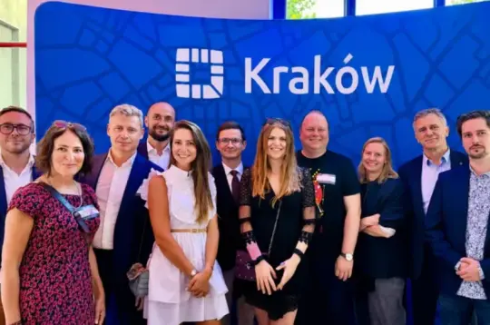 Grupa ludzi pozująca przed tłem z logo Krakowa.