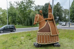Figurka jeźdźca na koniu z wikliny, umieszczona na rondzie w otoczeniu zieleni.