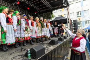 Grupa kobiet w tradycyjnych strojach ludowych śpiewa na scenie podczas festiwalu.